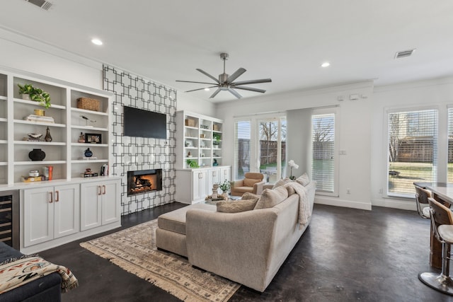 living room with ceiling fan, ornamental molding, a large fireplace, and a healthy amount of sunlight