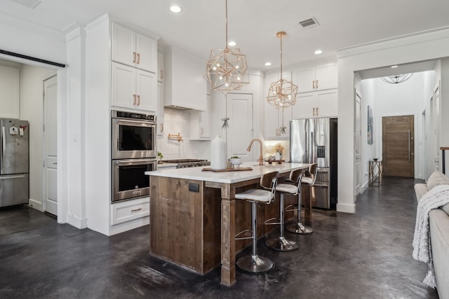 kitchen with appliances with stainless steel finishes, a kitchen island with sink, white cabinets, a kitchen bar, and decorative light fixtures