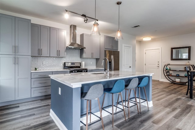 kitchen featuring light stone countertops, wall chimney exhaust hood, stainless steel appliances, sink, and a center island with sink