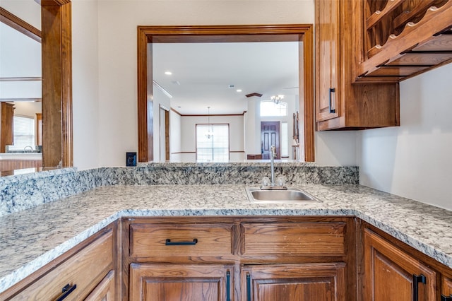 kitchen with ornamental molding, light stone countertops, brown cabinets, and a sink