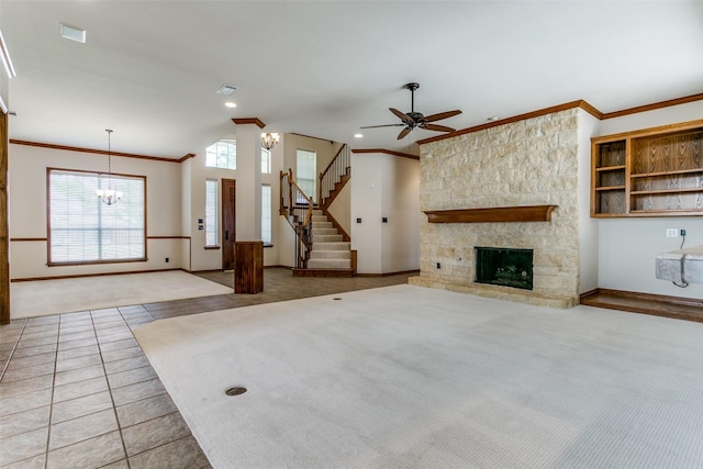 unfurnished living room featuring crown molding, ceiling fan with notable chandelier, light colored carpet, and a stone fireplace