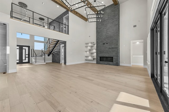 unfurnished living room with a towering ceiling, beamed ceiling, a fireplace, light wood-type flooring, and french doors