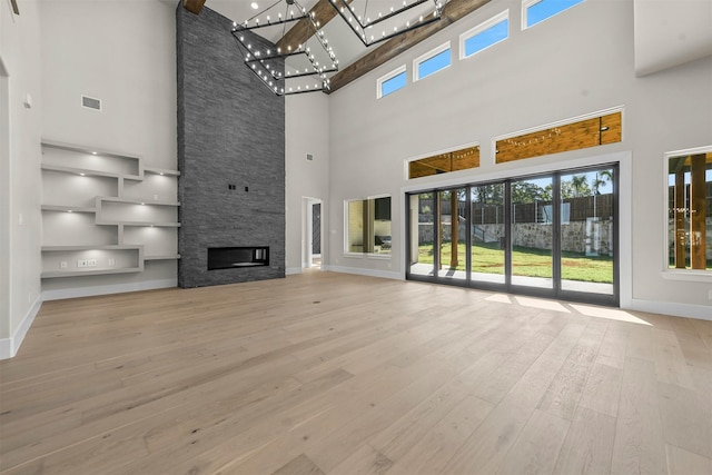 unfurnished living room with a towering ceiling, a stone fireplace, and light hardwood / wood-style flooring