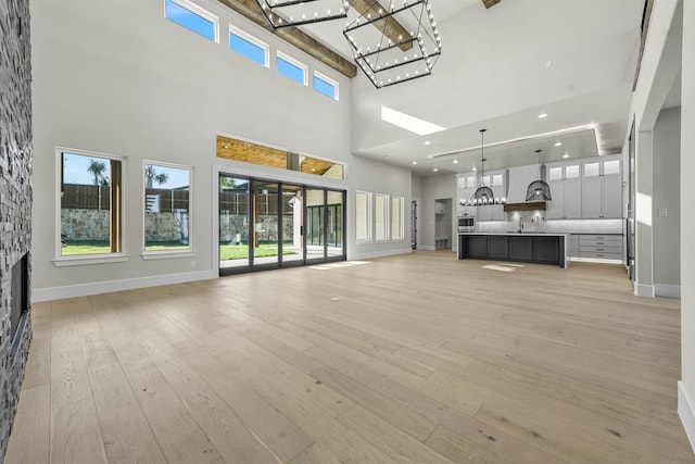 unfurnished living room featuring a high ceiling, an inviting chandelier, a fireplace, sink, and light hardwood / wood-style flooring