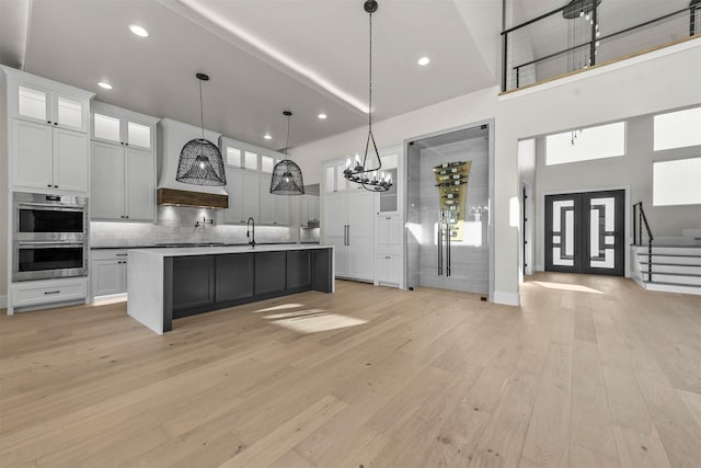 kitchen with pendant lighting, double oven, white cabinetry, a high ceiling, and an island with sink