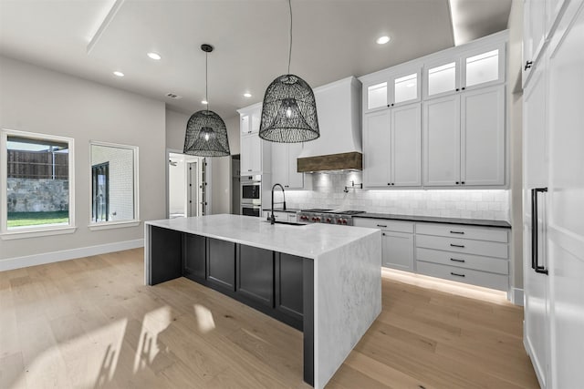 kitchen featuring hanging light fixtures, white cabinets, and an island with sink