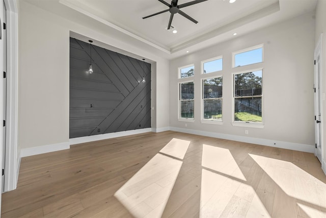 empty room featuring ceiling fan, a tray ceiling, and light wood-type flooring