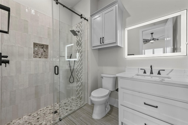 bathroom featuring toilet, a shower with shower door, ceiling fan, and vanity