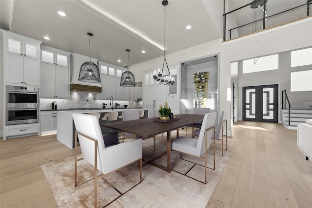 dining space with sink, a high ceiling, an inviting chandelier, and light hardwood / wood-style floors