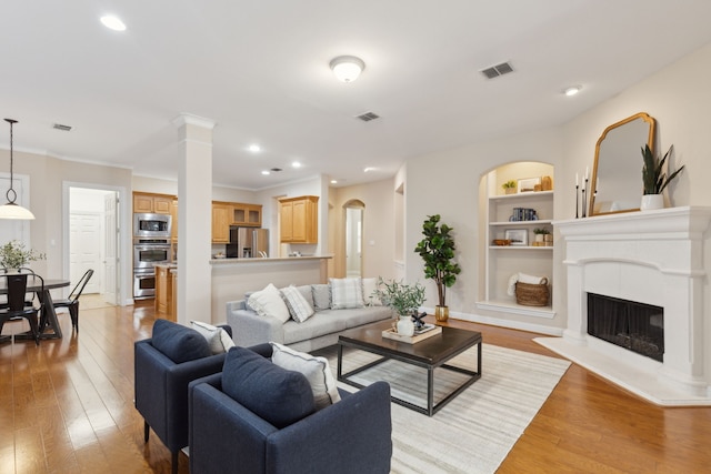 living room with built in shelves, light wood-type flooring, decorative columns, and ornamental molding