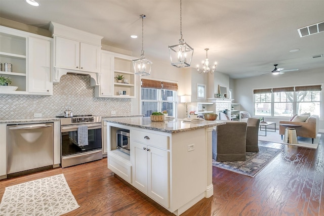 kitchen featuring appliances with stainless steel finishes, white cabinetry, light stone countertops, a center island, and range hood