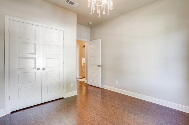 unfurnished bedroom featuring a closet, a notable chandelier, and dark wood-type flooring