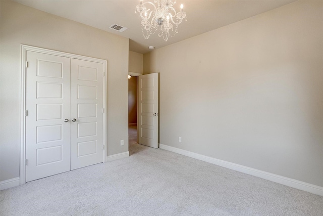 unfurnished bedroom featuring light colored carpet, a closet, and a notable chandelier