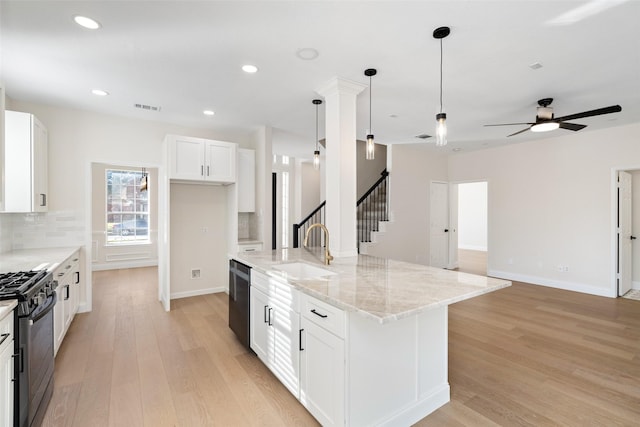 kitchen featuring hanging light fixtures, light stone countertops, black appliances, an island with sink, and white cabinets