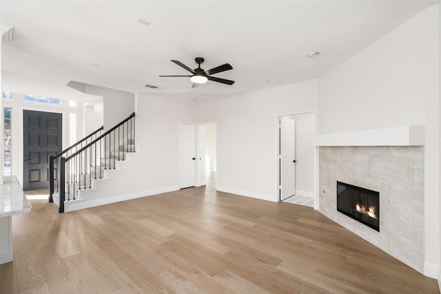 unfurnished living room with a tile fireplace, ceiling fan, and light hardwood / wood-style floors