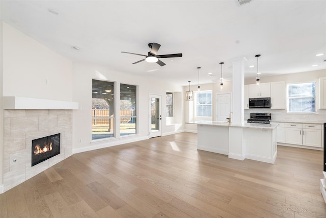 kitchen featuring appliances with stainless steel finishes, white cabinetry, light stone counters, light hardwood / wood-style floors, and a center island with sink