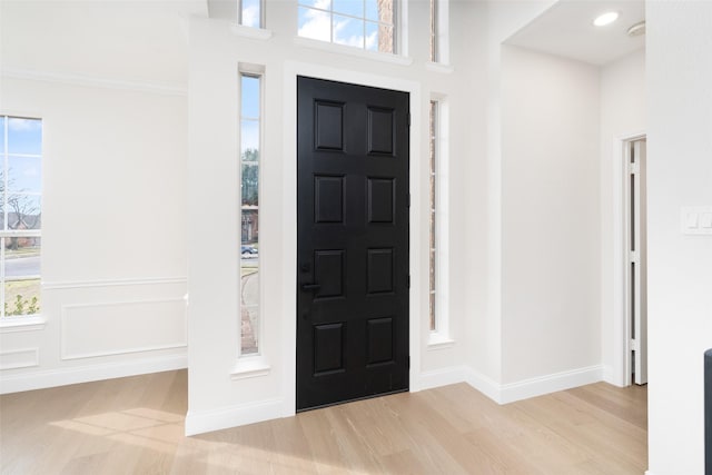 foyer with crown molding, a healthy amount of sunlight, and light wood-type flooring