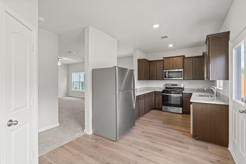 kitchen with dark brown cabinets, appliances with stainless steel finishes, sink, light colored carpet, and light stone counters