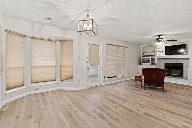 interior space with ceiling fan, light hardwood / wood-style floors, a textured ceiling, and a tiled fireplace