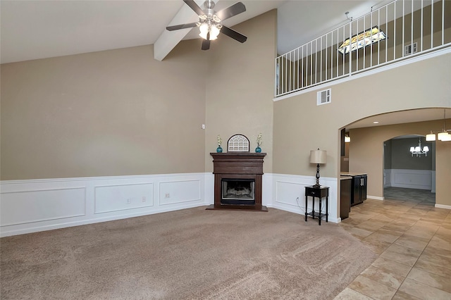 unfurnished living room with light carpet, beam ceiling, ceiling fan with notable chandelier, and high vaulted ceiling