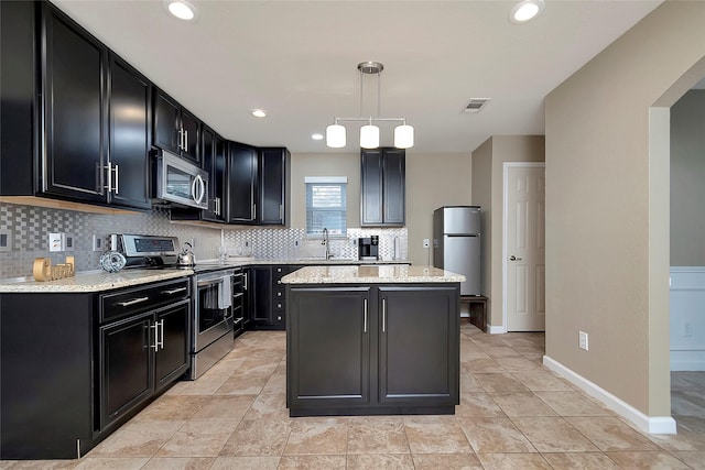 kitchen with pendant lighting, sink, appliances with stainless steel finishes, light stone counters, and a kitchen island