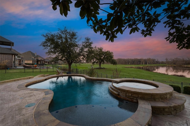 pool at dusk with a patio, an in ground hot tub, a water view, and a lawn