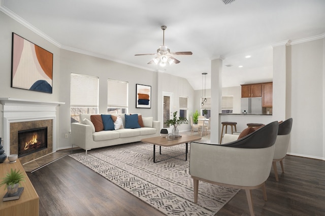 living room featuring vaulted ceiling, ornamental molding, dark wood-style flooring, and a tiled fireplace