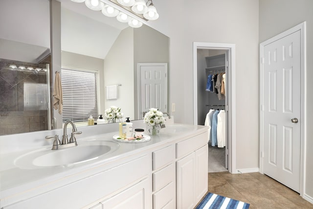 bathroom with vaulted ceiling, a sink, a tile shower, and double vanity