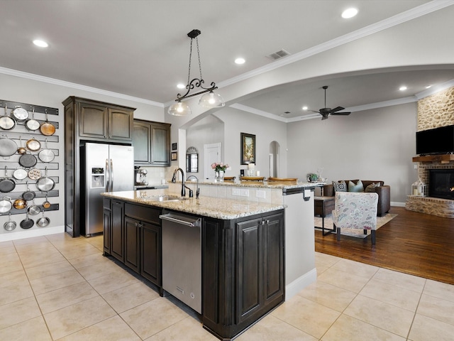 kitchen featuring sink, light tile patterned floors, appliances with stainless steel finishes, dark brown cabinetry, and a center island with sink