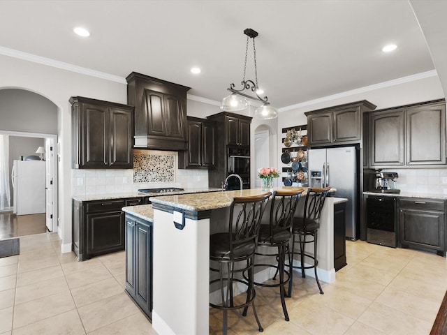 kitchen featuring light tile patterned flooring, dark brown cabinets, light stone countertops, and a center island with sink