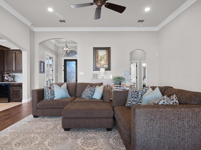 living room with ceiling fan with notable chandelier, ornamental molding, beverage cooler, and light wood-type flooring