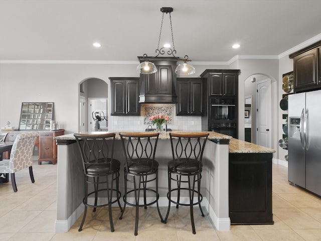 kitchen with premium range hood, stainless steel fridge with ice dispenser, a center island with sink, pendant lighting, and backsplash