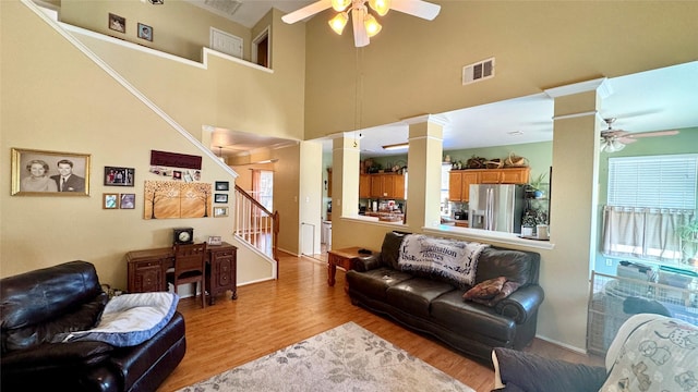 living room with decorative columns, a high ceiling, ceiling fan, and light wood-type flooring