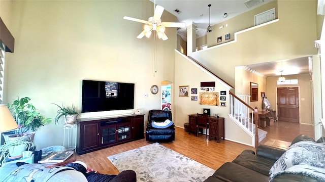 living room featuring light hardwood / wood-style flooring, a towering ceiling, ceiling fan, and ornamental molding