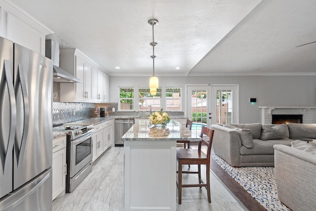 kitchen with light stone counters, stainless steel appliances, white cabinets, open floor plan, and hanging light fixtures