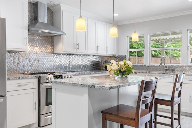 kitchen featuring wall chimney exhaust hood, stainless steel range oven, a breakfast bar area, and white cabinetry