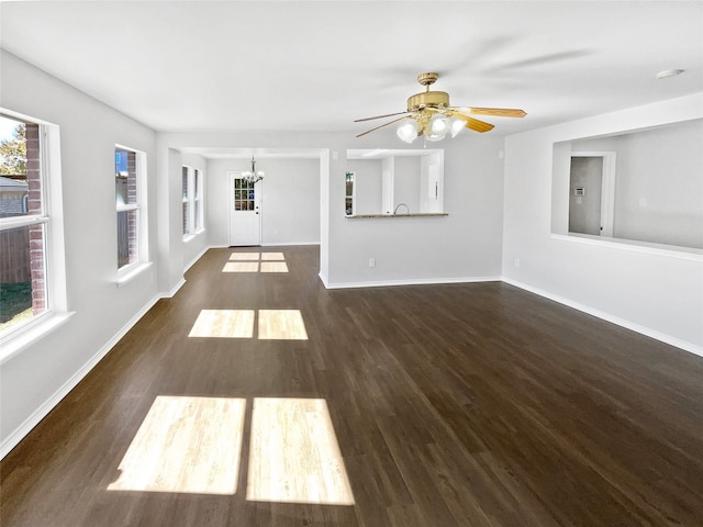 unfurnished living room with ceiling fan with notable chandelier, a wealth of natural light, and dark hardwood / wood-style floors