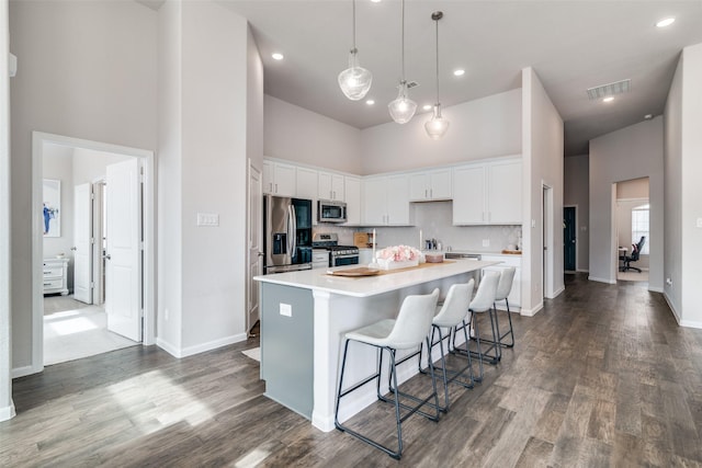 kitchen with appliances with stainless steel finishes, a towering ceiling, white cabinetry, a kitchen breakfast bar, and a center island