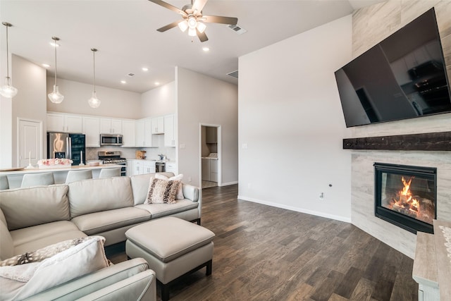 living room featuring dark wood-type flooring, ceiling fan, a fireplace, and a high ceiling