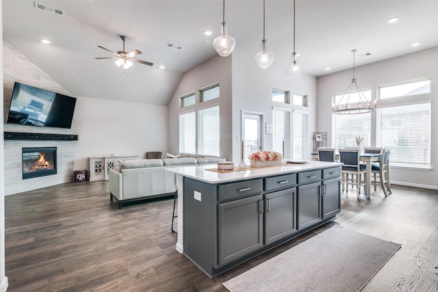 kitchen with dark wood-type flooring, gray cabinetry, a fireplace, a kitchen island, and decorative light fixtures