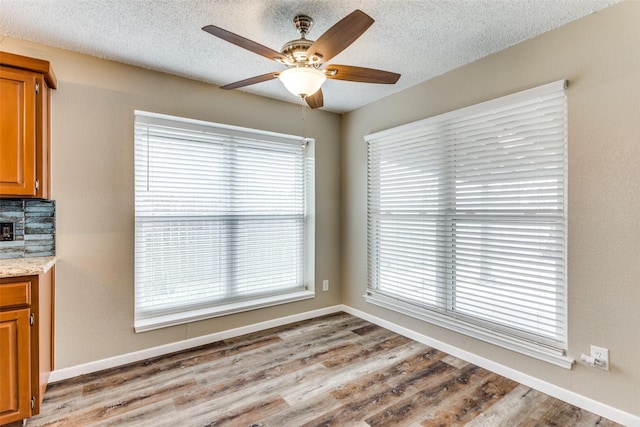 unfurnished dining area with ceiling fan, a textured ceiling, and light wood-type flooring