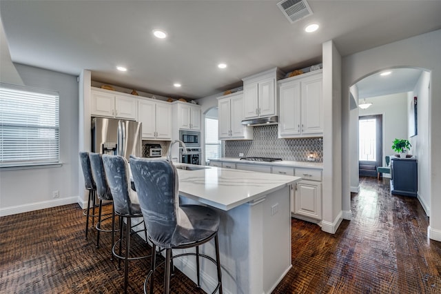 kitchen with stainless steel appliances, white cabinetry, a breakfast bar, and an island with sink