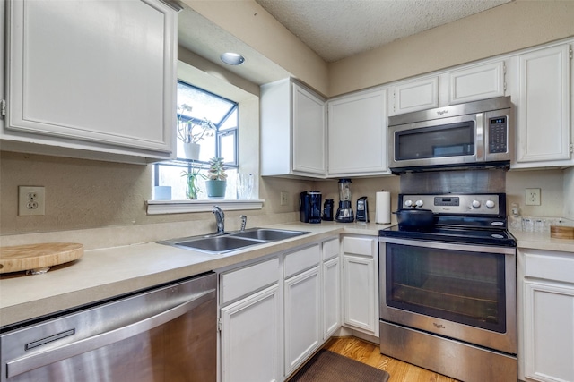 kitchen with stainless steel appliances, a textured ceiling, light countertops, white cabinetry, and a sink