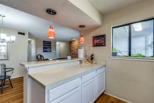 kitchen with dark wood-style floors, decorative light fixtures, visible vents, a textured ceiling, and a peninsula