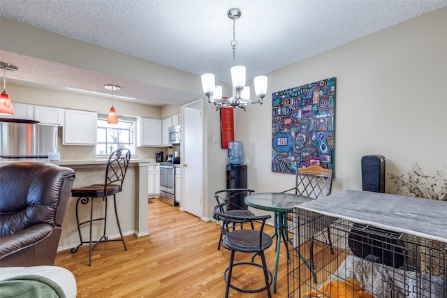 dining area with light hardwood / wood-style floors, a textured ceiling, and a notable chandelier