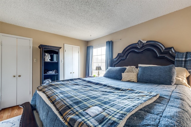 bedroom featuring two closets, wood-type flooring, and a textured ceiling