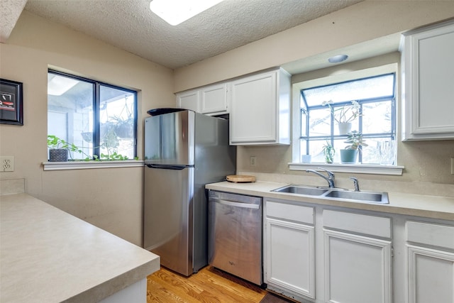 kitchen featuring white cabinets, appliances with stainless steel finishes, a sink, light countertops, and a wealth of natural light