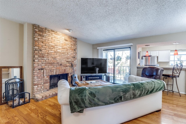 living room featuring a brick fireplace, plenty of natural light, light wood-style flooring, and a textured ceiling