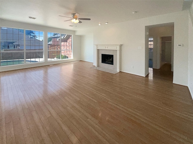 unfurnished living room with hardwood / wood-style floors, a tile fireplace, and ceiling fan