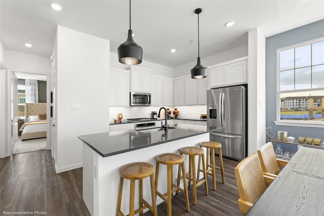 kitchen with appliances with stainless steel finishes, white cabinets, decorative light fixtures, sink, and dark wood-type flooring